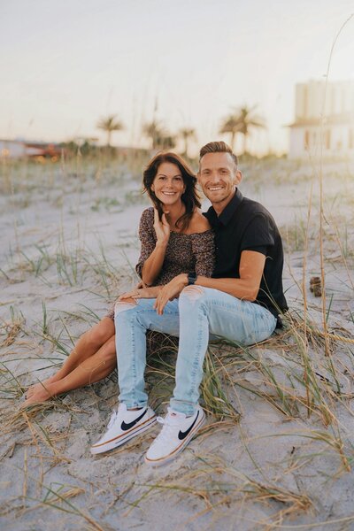 husband and wife sitting on beach smiling