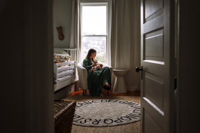 mom sitting in a chair by the window at home nursing baby