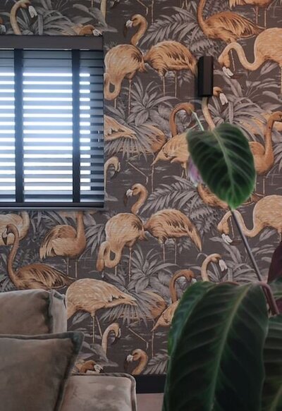 Close-up van flamingo behang met groene planten en deel van beige bank in tropisch geïnspireerd interieur