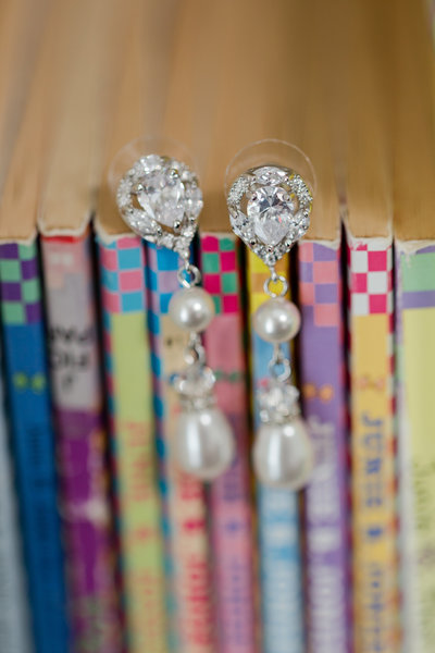Colorful books lined on a shelf with rhinestone and pearl earrings