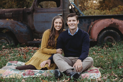 A couple posing on a blanket with an old truck.
