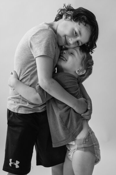 Black and white photo of boy sibilings hugging each other in white studio in Annapolis Maryland.