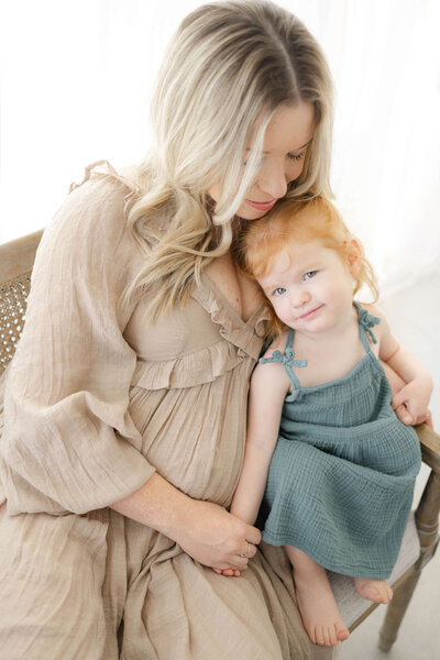 Mother cuddling and holding hands with her beautiful red headed daughter in an Oklahoma City Metro photography studio.