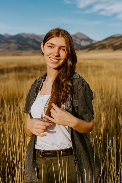 A senior session in a golden field with mountains in the background.