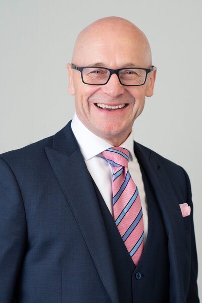 A corporate headshot showing a bald man in a blue 3 piece suit and pink tie.  Captured in studio by Ottawa Event Photographer JEMMAN Photography COMMERCIAL