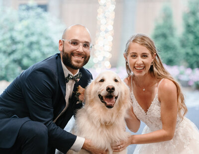 A joyful scene on the wedding day as a beaming couple, dressed elegantly, poses with their beloved dog
