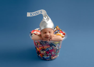Newborn dressed as a kiss candy sitting in a bowl of candy.