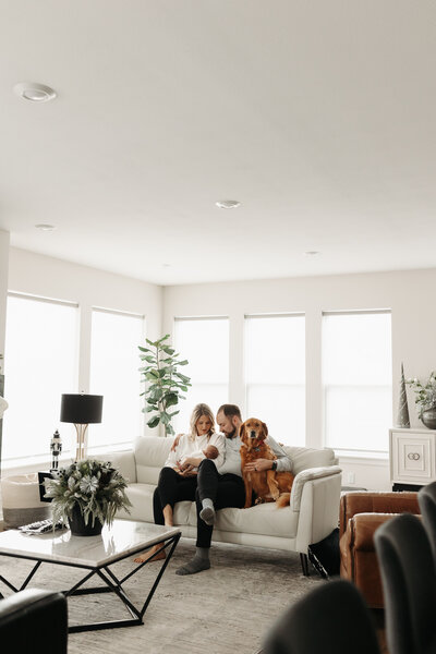 Woman Man and dog sitting on couch holding newborn baby