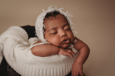 Newborn baby girl asleep posed in basket at atlanta newborn photography studio propped up on elbows with chin in hands