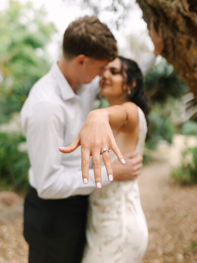 bride showing her engagement ring to the camera underneath a willow tree in balboa park san diego