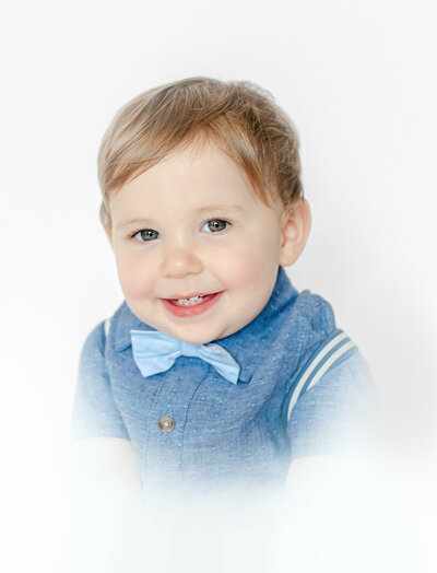 one year old boy wearing a denim shirt with bowtie and suspenders with white border around him by harrisburg pa photographer