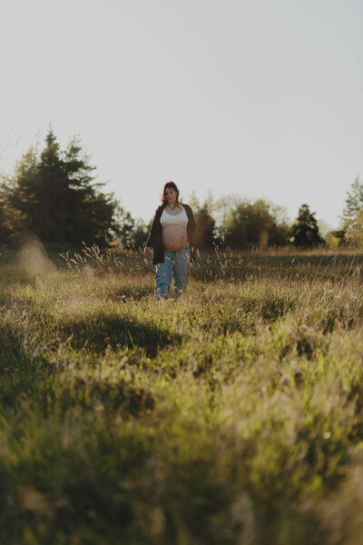 Gravidbild på en gravid kvinna gåendes i högt gräs under en gravidfotografering