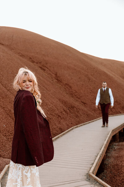 Bride wearing groom's jacket as he walks towards her.