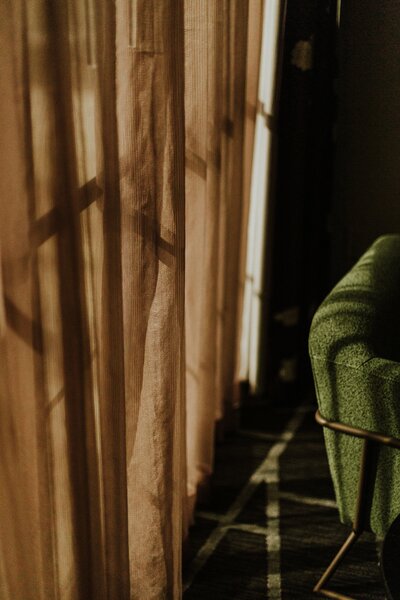 A green velvet chair in front of a brown curtain covering a window