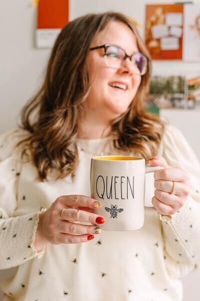 Woman holding a coffee cup that says queen and has a bumble bee on it