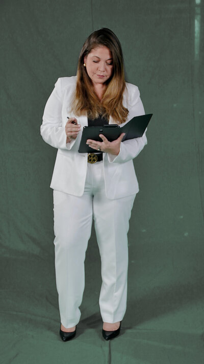 Teresa Cordoba stands in a white pantsuit while writing in a notebook or tablet.