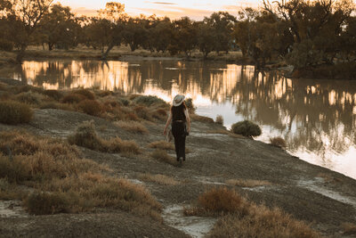 woman walking through a field at sunset in a cowboy hat