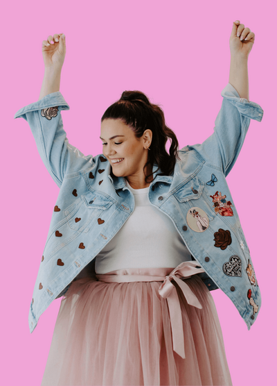 woman dark hair with arms up celebrating in jean jacket and pink skirt