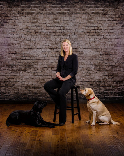 A personal branding photo of a woman with her two dogs on a brick background