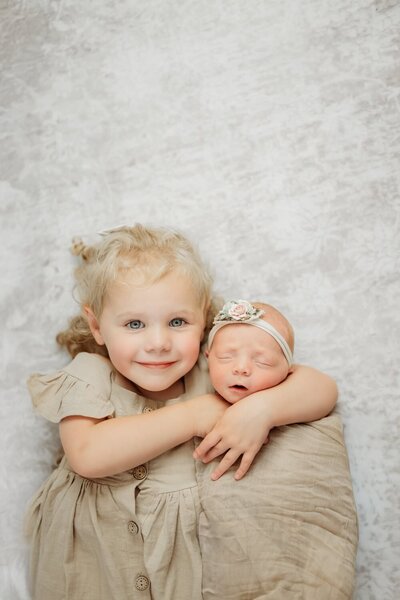 newborn baby girl wrapped in her sisters arms as they look up at camera