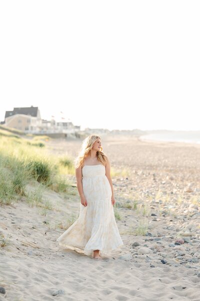 teen girl wearing a white dress walking on the beach