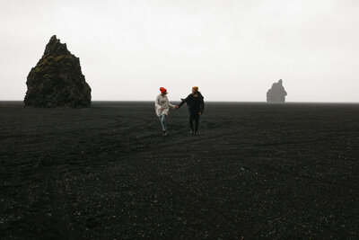 couple holding hands and running over black sand beach in Iceland