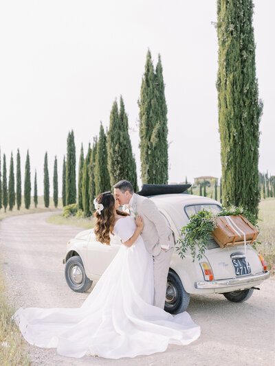 Bride and groom kiss in front of fiat in Tuscany, Italy