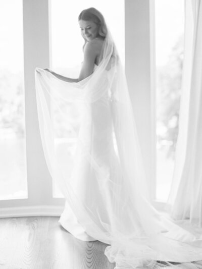 Rhode Island Wedding photographer | A bride stands gracefully in front of large windows, her white dress and veil flowing elegantly. 