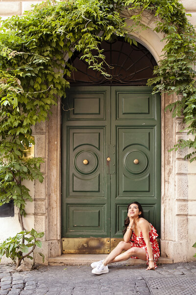 A girl traveling solo in Rome sitting in front of a green door with Ivy in Trastevere. Taken by Rome Portrait Photographer, Tricia Anne Photography