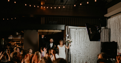 Bride and groom enter room for first time at reception to welcoming cheers from friends and family