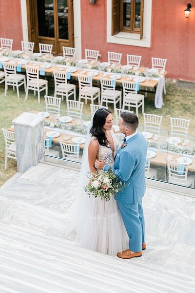 Bride and groom share an intimate moment on the marble steps of Villa Veneziano in Lefkada, surrounded by a chic outdoor tablescape