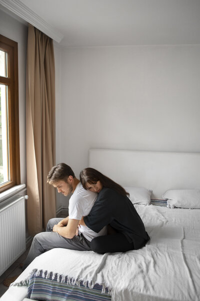 A woman hugging a mans  back while both look upset. Representing partners that could benefit from couples therapy with a marriage counselor in Brooklyn, NY. A couples therapist can help you resolve your disagreements.