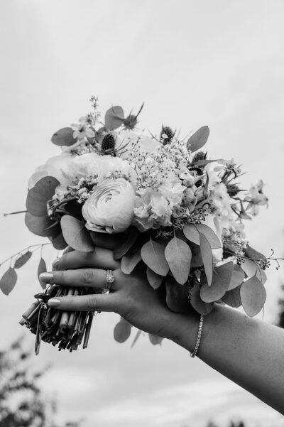 Black and white photo of a hand holding an elegant bridal bouquet featuring roses, eucalyptus leaves, and delicate flowers at Empress Estate.