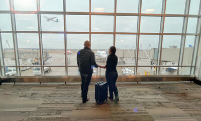 minneapoliis wedding videographer couple, flor and ariel, look out the aiport window while a plane flies off