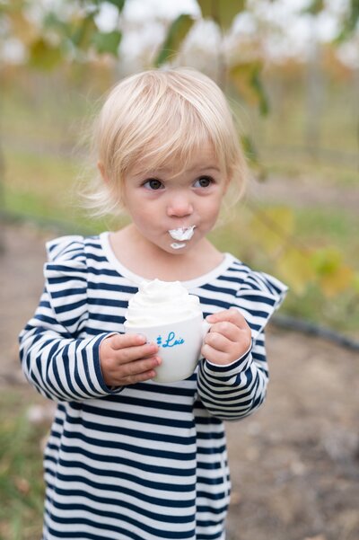 a toddler enjoying a small mug of hot cocoa topped with whipped cream