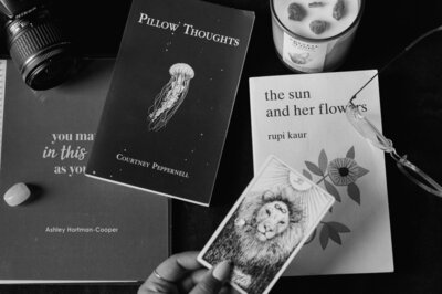 A scattered array of items including a candle with crystals, glasses, tarot card for strength, with a lion. Pillow Thoughts, by Rupi Karu, and a "you matter, in this space, as you are." Ashley Hortman-Cooper by Erin Condrin.