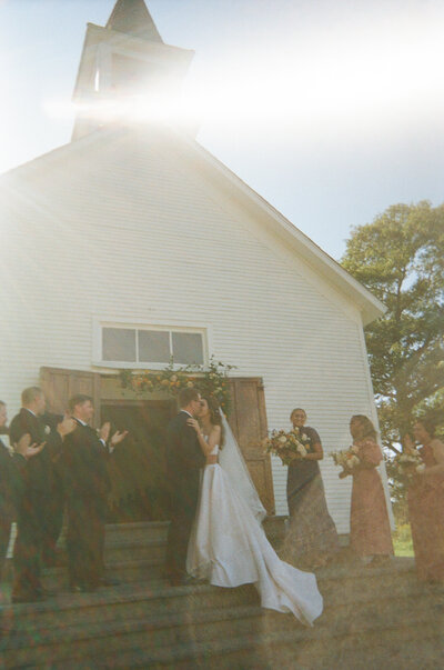 a bride and groom share their first kiss on the steps of a little white chapel