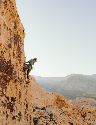 woman rock climbing with mountains in the background