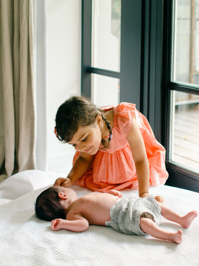 Big sister gazes lovingly at her newborn sister during her newborn shoot.