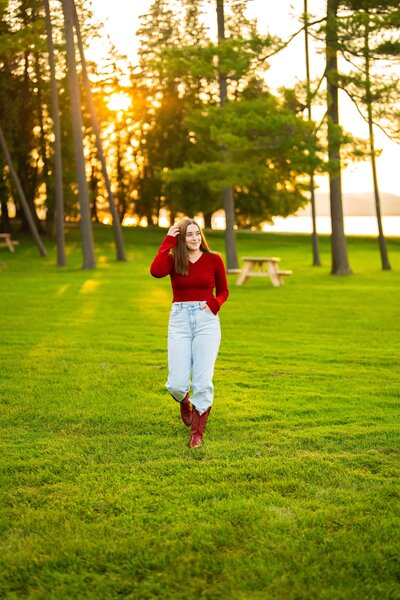 High school senior girl walking in a park at sunset, wearing a red sweater and jeans.
