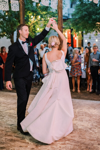 Groom spinning bride while they dance outside in front of wedding guests