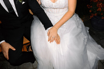 A bride in a white wedding dress and a groom in a black suit sit closely together, their rings visible, beautifully captured by a film photographer NJ—perfectly preserving this tender newlywed moment.
