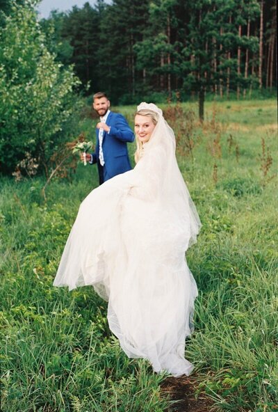 minnesota wedding photography by tom thornton of bride looking back at camera while she and groom walk through lush grassy field