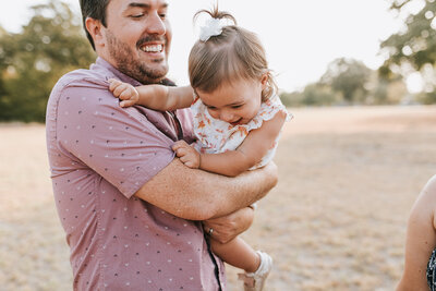 Experience the joy of family bonding in North Texas as a father and daughter create cherished memories in this delightful photograph. Captured against the picturesque backdrop of North Texas, this heartwarming image portrays the playful interaction between a doting father and his daughter. Witness the genuine laughter and connection as they engage in playful activities, illustrating the warmth and love within this family moment. Professional family photography that encapsulates the joy and closeness shared by a father and daughter in North Texas