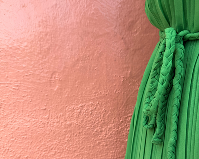 Green dress with a knotted bow in front of the pinkish peach wall. 