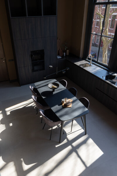 Gemeubileerde en ruime loft in het centrum van Groningen met zwarte tafel en stoelen en ontbijt op tafel. Zonlicht door hoge ramen.