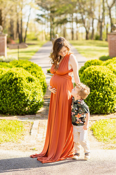 Mom to be in an orange dress standing in a garden