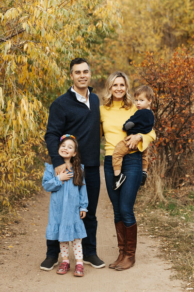 Two parents smiling as one holds a small child and another has a child standing in front of them.