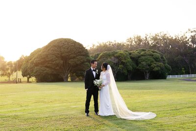 A newlywed couple standing close and smiling at each other at sunset 