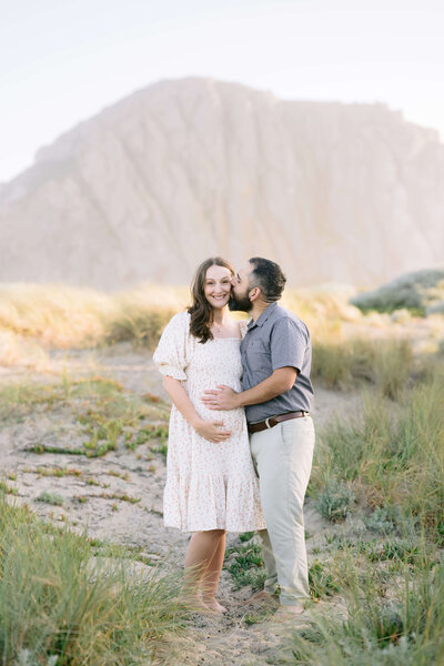Expecting mother with her husband kissing her in front of Morro Rock